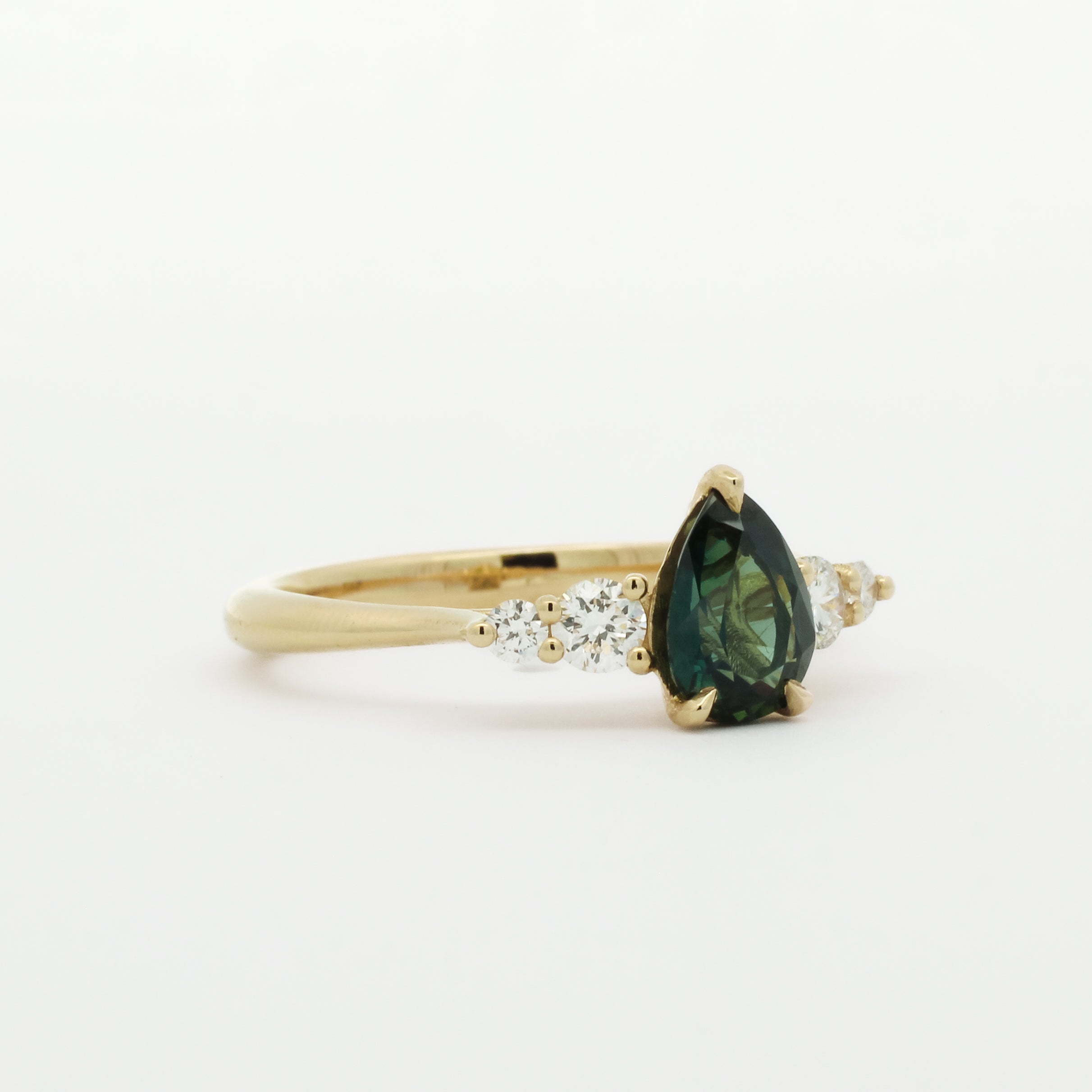 Gold engagement ring with a pear shaped green gemstone and smaller diamonds on a white background