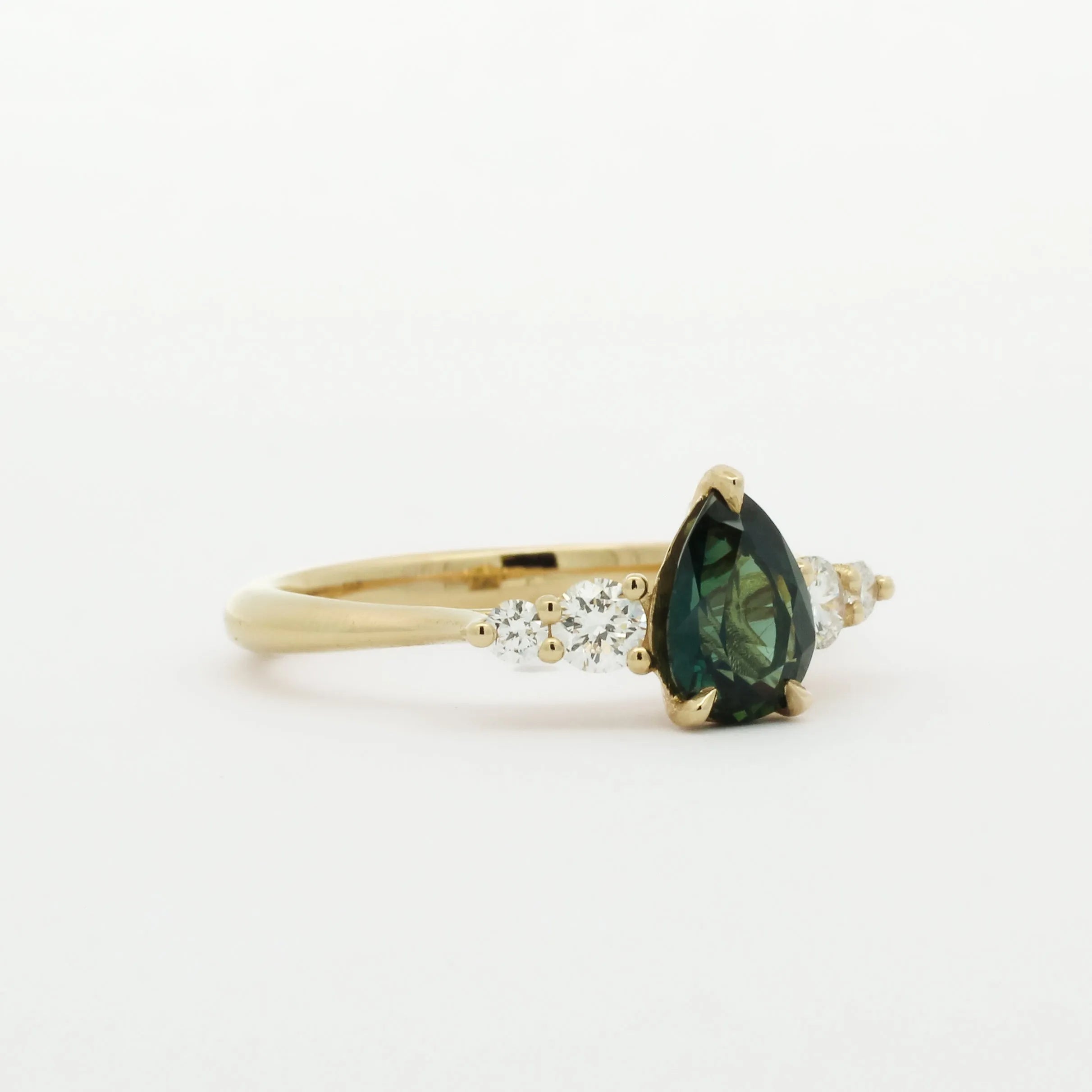 Gold engagement ring with a pear shaped green gemstone and smaller diamonds on a white background