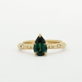 Gold ring with a green pear sapphire and diamonds in star engraving on a white background