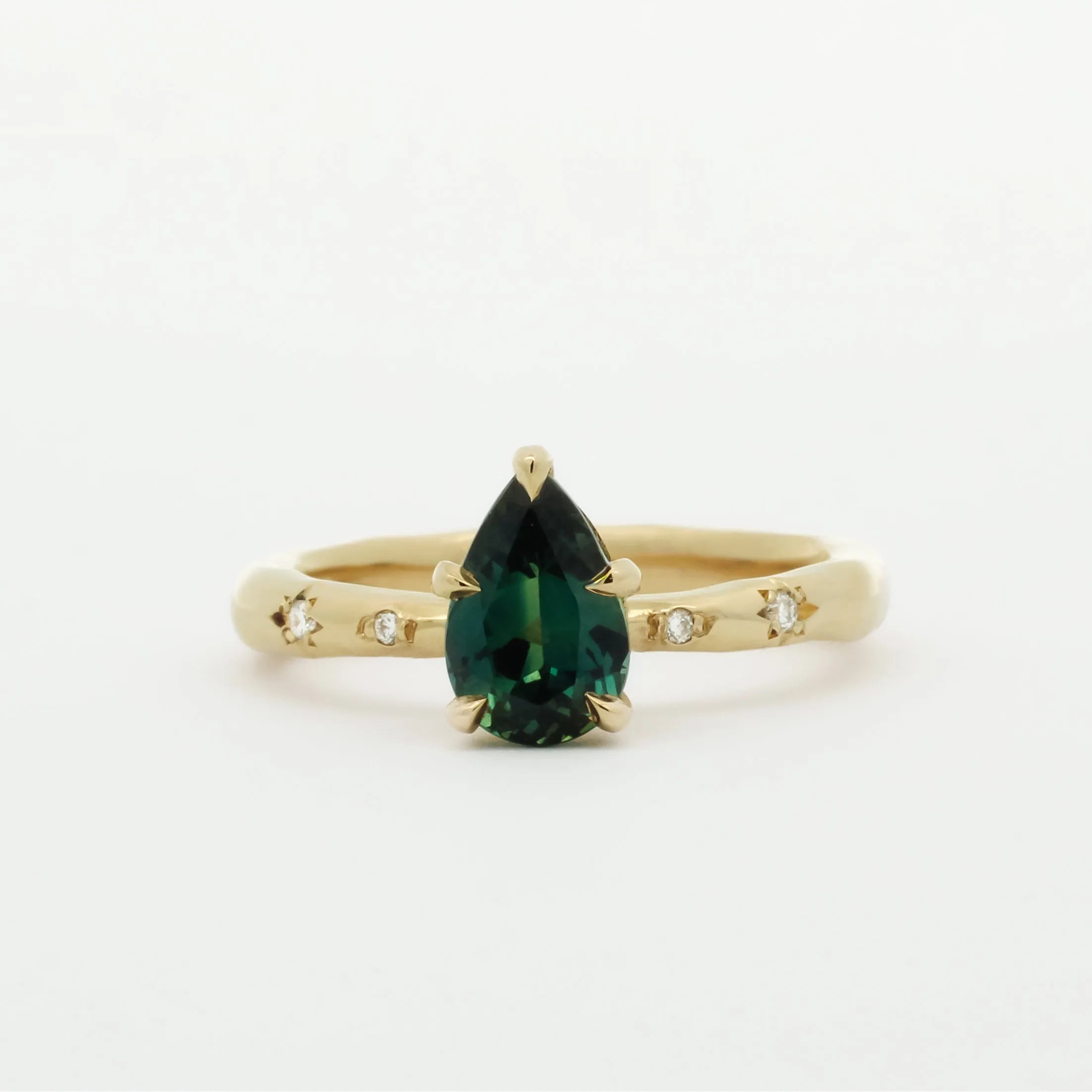 Gold ring with a green pear sapphire and diamonds in star engraving on a white background