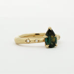 side view of gold engagement ring with organic band, star-set diamonds and a green pear gemstone on a white background