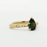 side view of gold engagement ring with organic band, star-set diamonds and a green pear gemstone on a white background