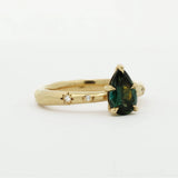 side view of gold engagement ring with organic band, star-set diamonds and a green pear gemstone on a white background