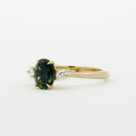 side view of gold engagement ring with a green gemstone on a white background