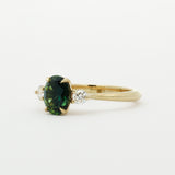 side view of gold engagement ring with a green gemstone on a white background