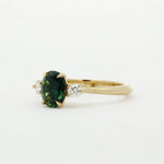 side view of gold engagement ring with a green gemstone on a white background
