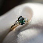 trilogy engagement ring with peacock blue green oval sapphire in blurred neutral fabric