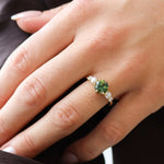 close up of hand wearing a bright green blue round parti sapphire engagement ring with round diamonds