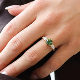 close up of hand wearing a bright green blue round parti sapphire engagement ring with round diamonds