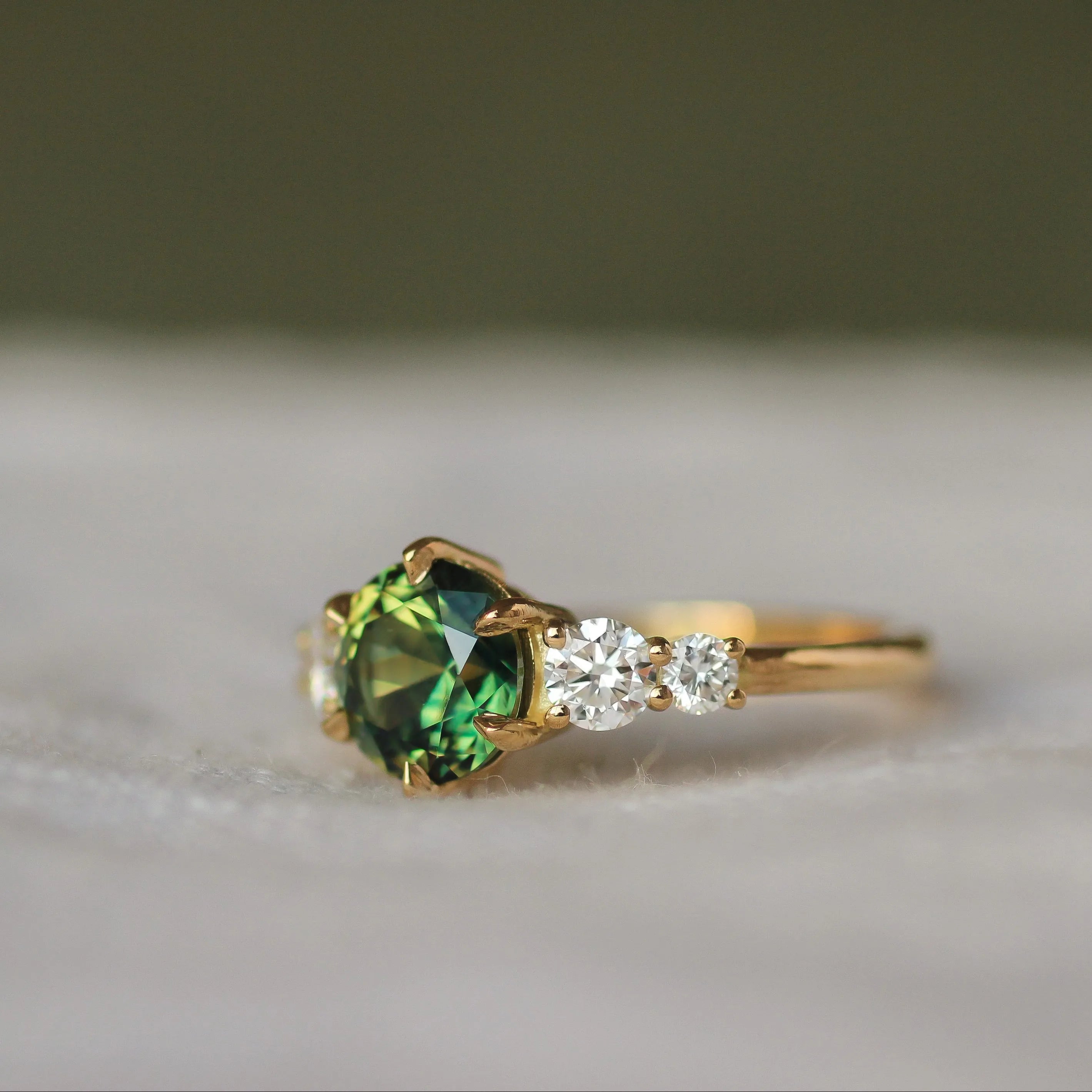 Gold engagement ring with a round vibrant green sapphire and small diamonds on a neutral blurred background