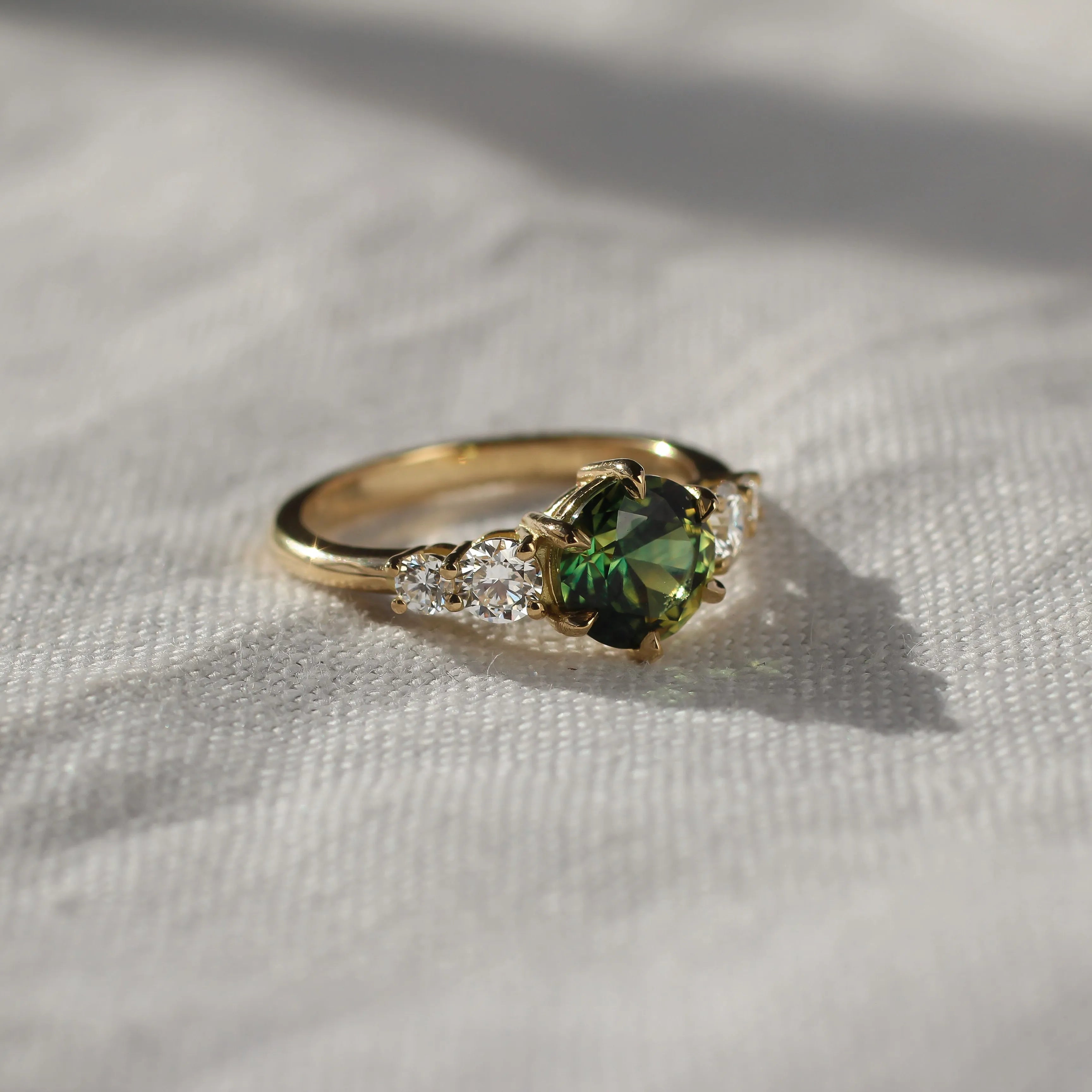 Gold ring with a green gemstone on a light fabric background in the sun