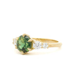 Gold ring with a round green blue sapphire and smaller diamonds on a white background