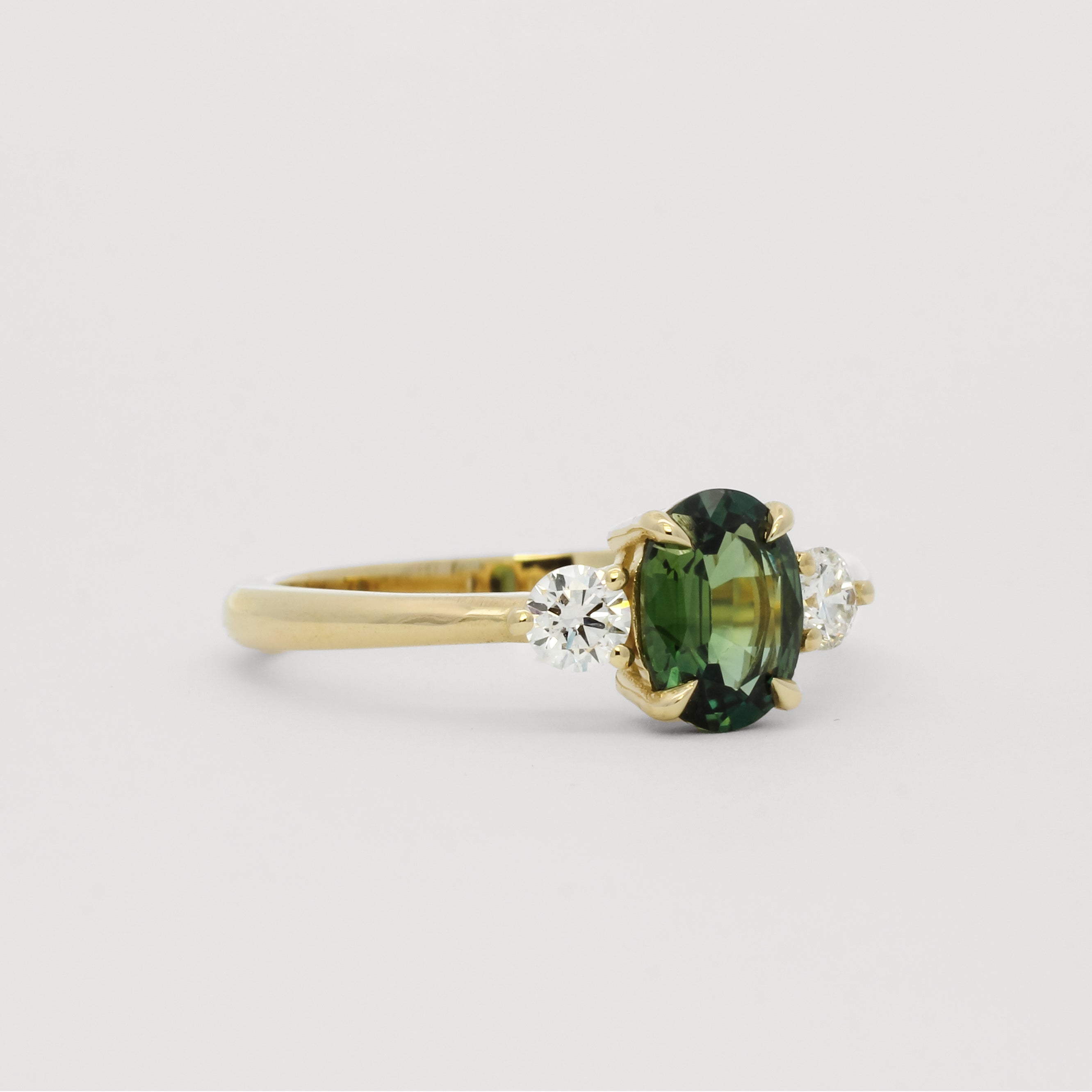 side view of 9 carat gold engagement ring with green sapphire and round diamonds low-set