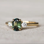 Gold trilogy engagement ring with a oval green gemstone and round diamonds on a textured surface