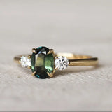Gold trilogy engagement ring with a oval green gemstone and round diamonds on a textured surface