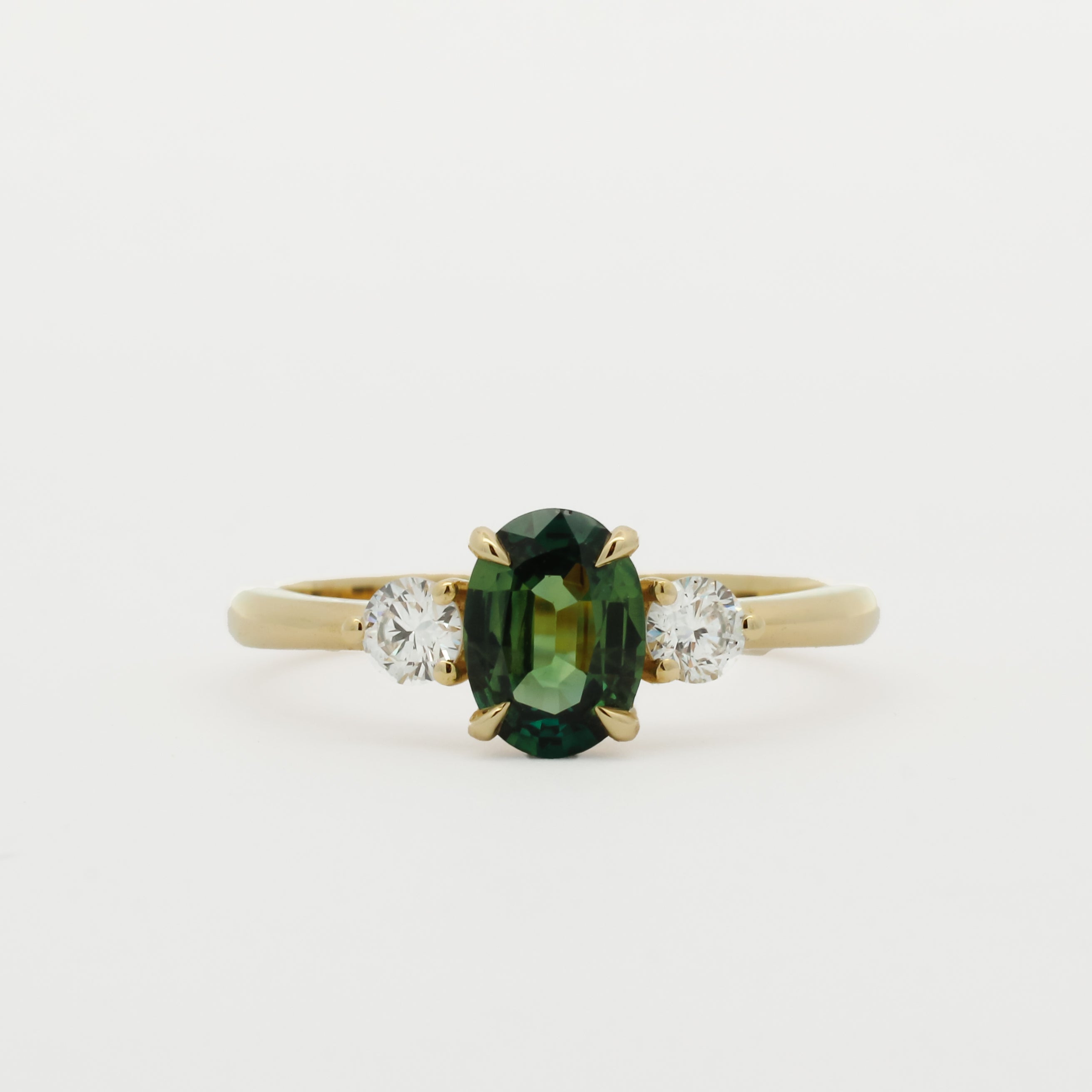 three stone engagement ring with green oval sapphire and 3mm diamonds on a white background