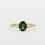 three stone engagement ring with green oval sapphire and 3mm diamonds on a white background