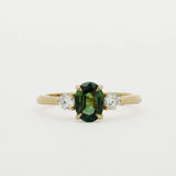 three stone engagement ring with green oval sapphire and 3mm diamonds on a white background