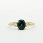 Gold ring with a green gemstone and two smaller diamonds on a white background