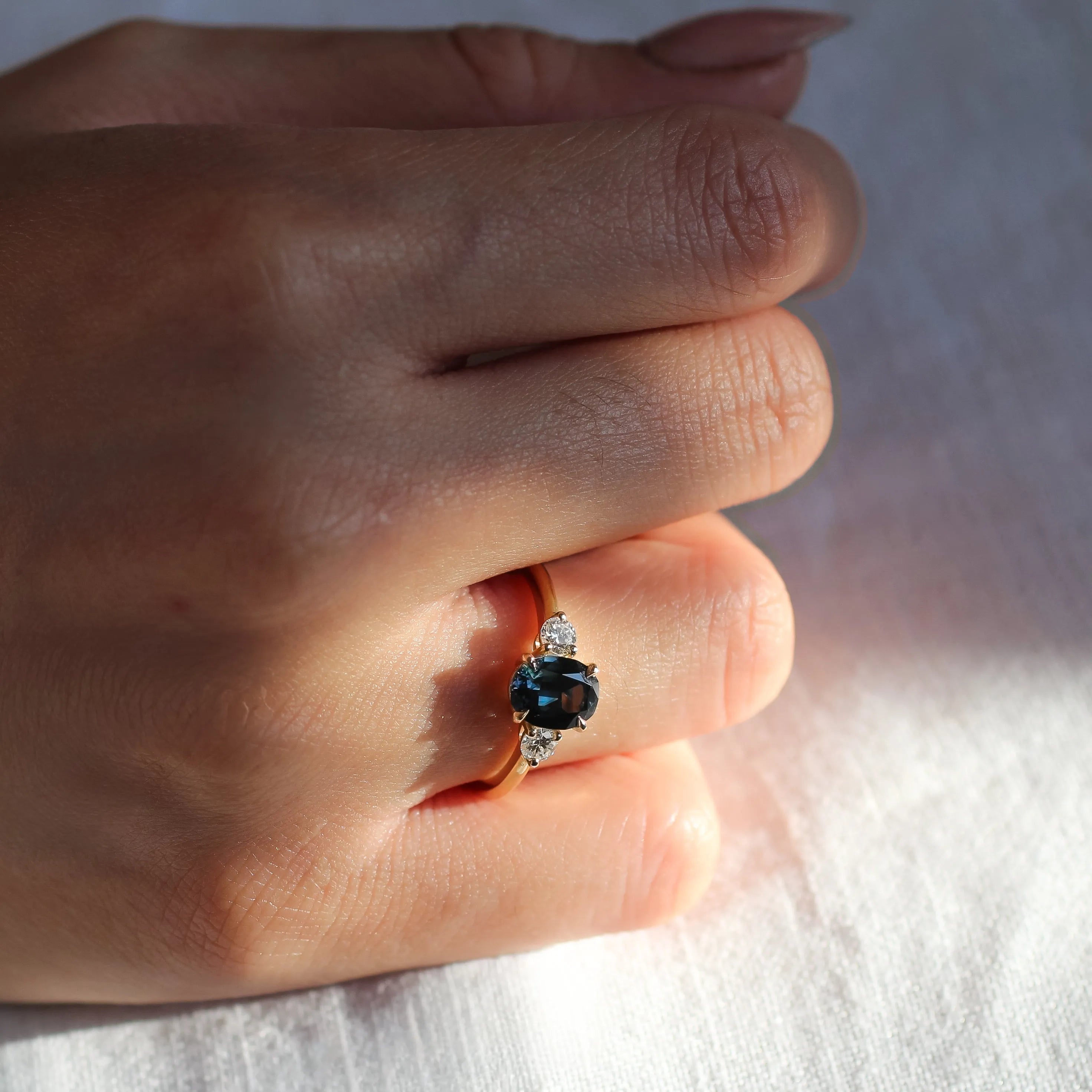 engagement ring with blue oval sapphire and round diamonds worn on hand in sunlight