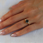 blue sapphire engagement ring with diamonds on a hand resting on white fabric