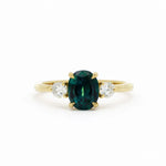Gold engagement ring with a greeny blue sapphire and two smaller diamonds on a white background