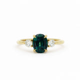 Gold engagement ring with a greeny blue sapphire and two smaller diamonds on a white background
