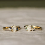 Two gold rings with diamond and blue and green sapphire stones on a textured surface