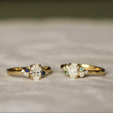 Two gold rings with diamond and blue and green sapphire stones on a textured surface