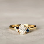 dainty gold engagement ring with a diamond and smaller blue sapphires on a textured surface