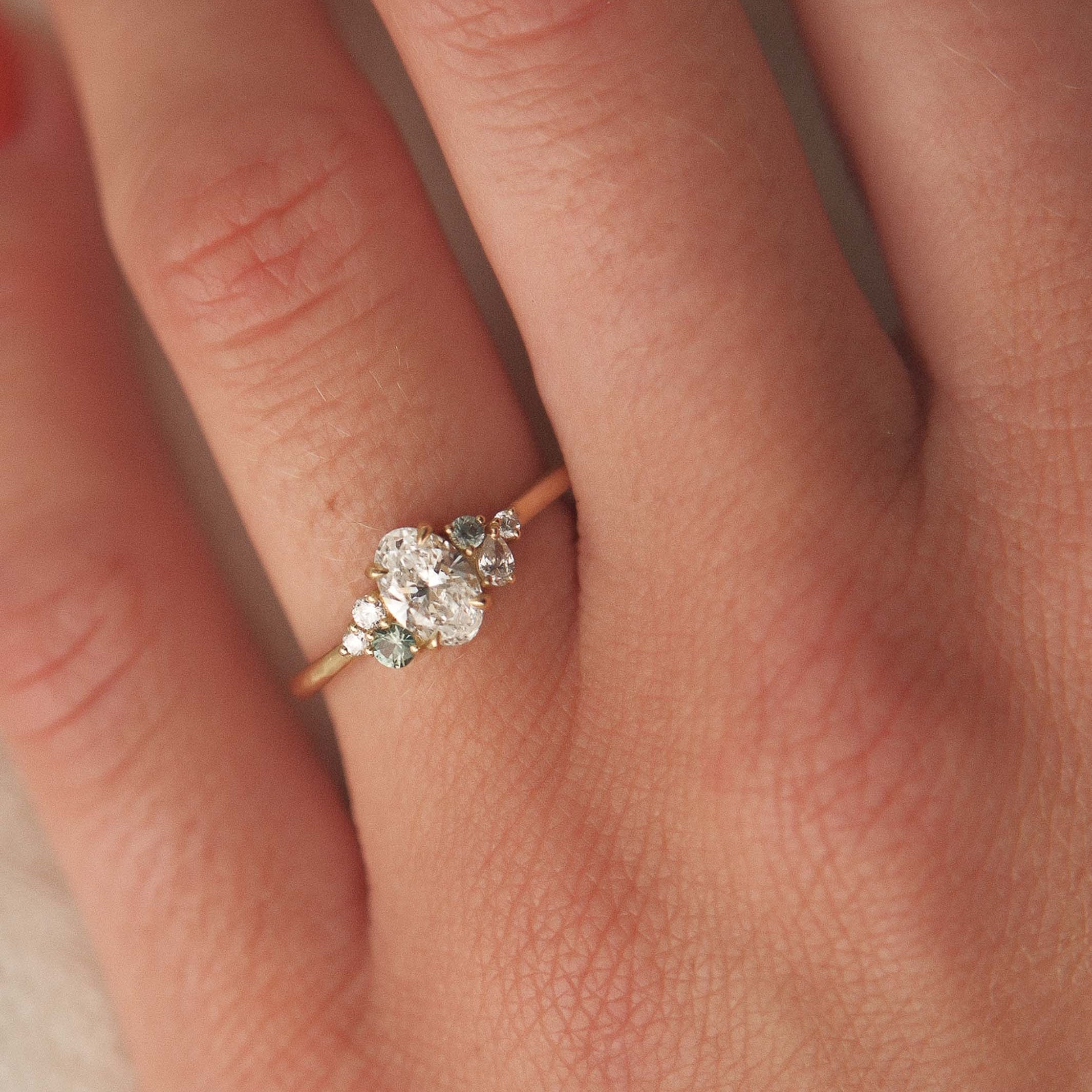 Close-up of a hand wearing a diamond ring with small green sapphires with a soft focus background
