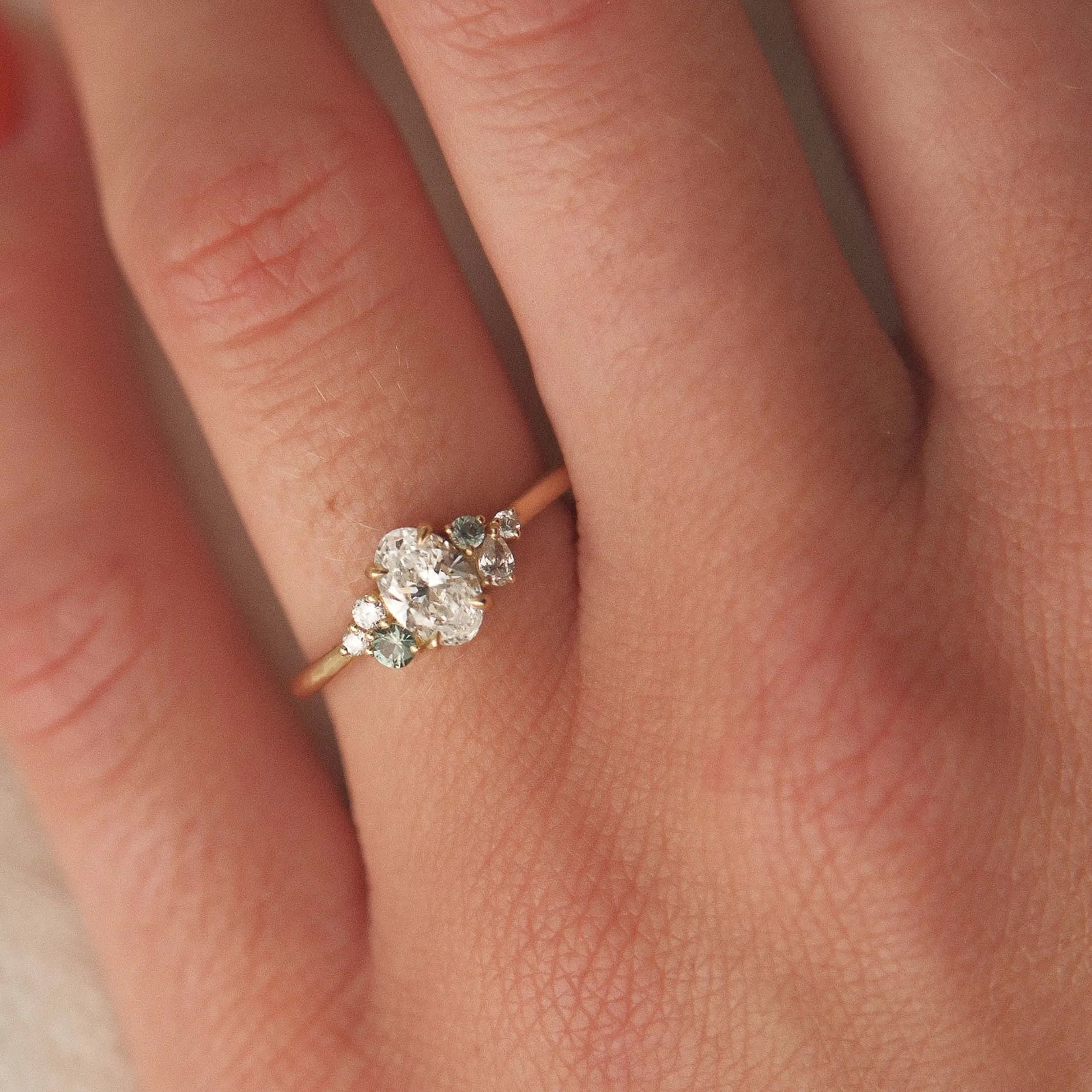 Close-up of a hand wearing a diamond ring with small green sapphires with a soft focus background