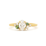 yellow gold diamond engagement ring with oval centre stone with round and pear accent diamonds and round green sapphires on a white background