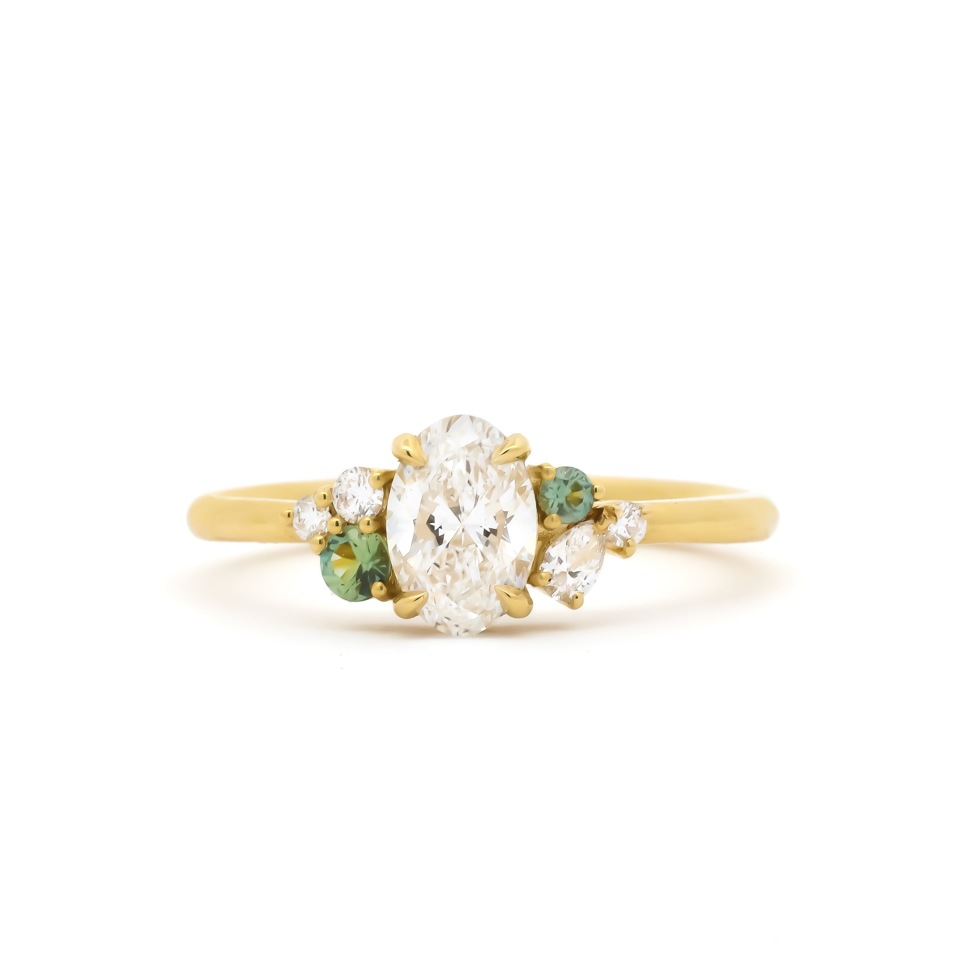 yellow gold diamond engagement ring with oval centre stone with round and pear accent diamonds and round green sapphires on a white background