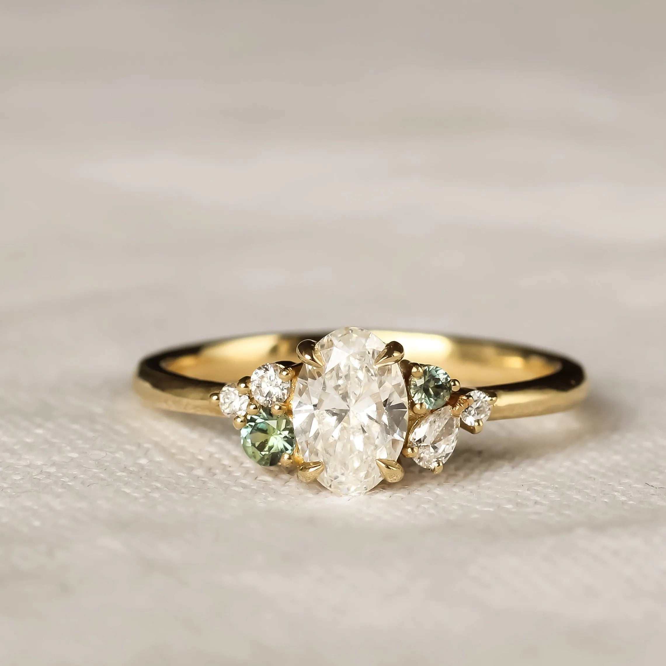 Gold ring with diamonds and green sapphires on a textured beige surface