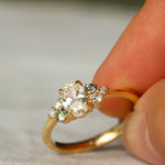 Gold ring with diamonds and small green sapphires held between fingers on a neutral background