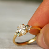 Gold ring with diamonds and small green sapphires held between fingers on a neutral background