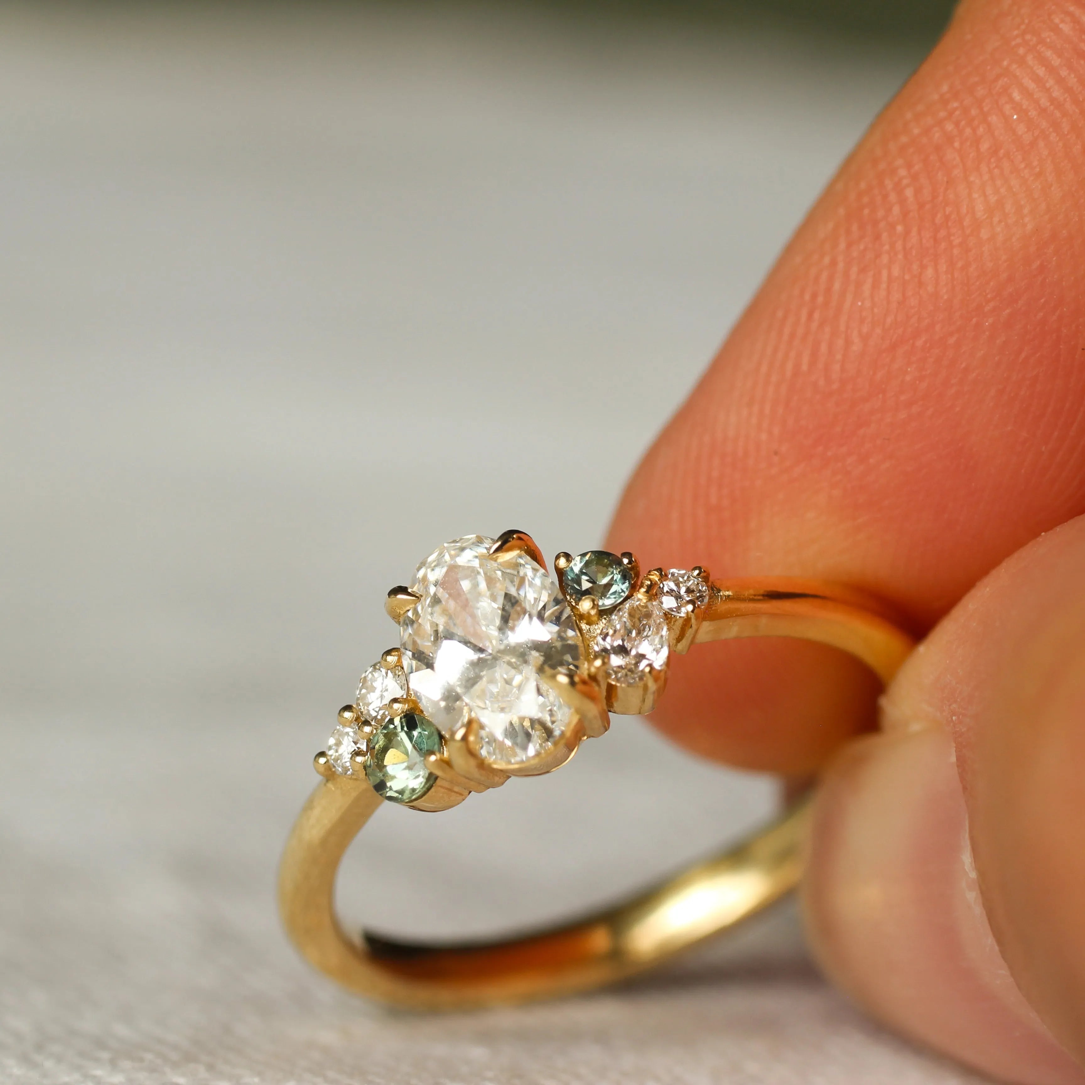 Gold ring with diamonds and small green sapphires held between fingers on a neutral background