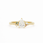 Gold ring with a pear-shaped diamond and smaller gemstones on a white background