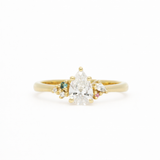 Gold ring with a pear-shaped diamond and smaller gemstones on a white background