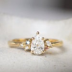 Gold ring with a pear-shaped diamond and small blue and pink sapphires on a textured surface