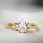 Gold ring with a pear-shaped diamond and small blue and pink sapphires on a textured surface
