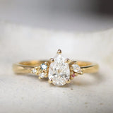 Gold ring with a pear-shaped diamond and small blue and pink sapphires on a textured surface