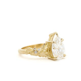 Gold ring with a large pear diamond and smaller diamonds with leaves engraved detail on a white background