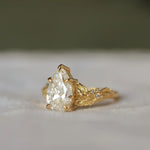 gold pear diamond engagement ring with leaf detail and round diamonds with a blurred background