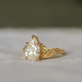 gold pear diamond engagement ring with leaf detail and round diamonds with a blurred background