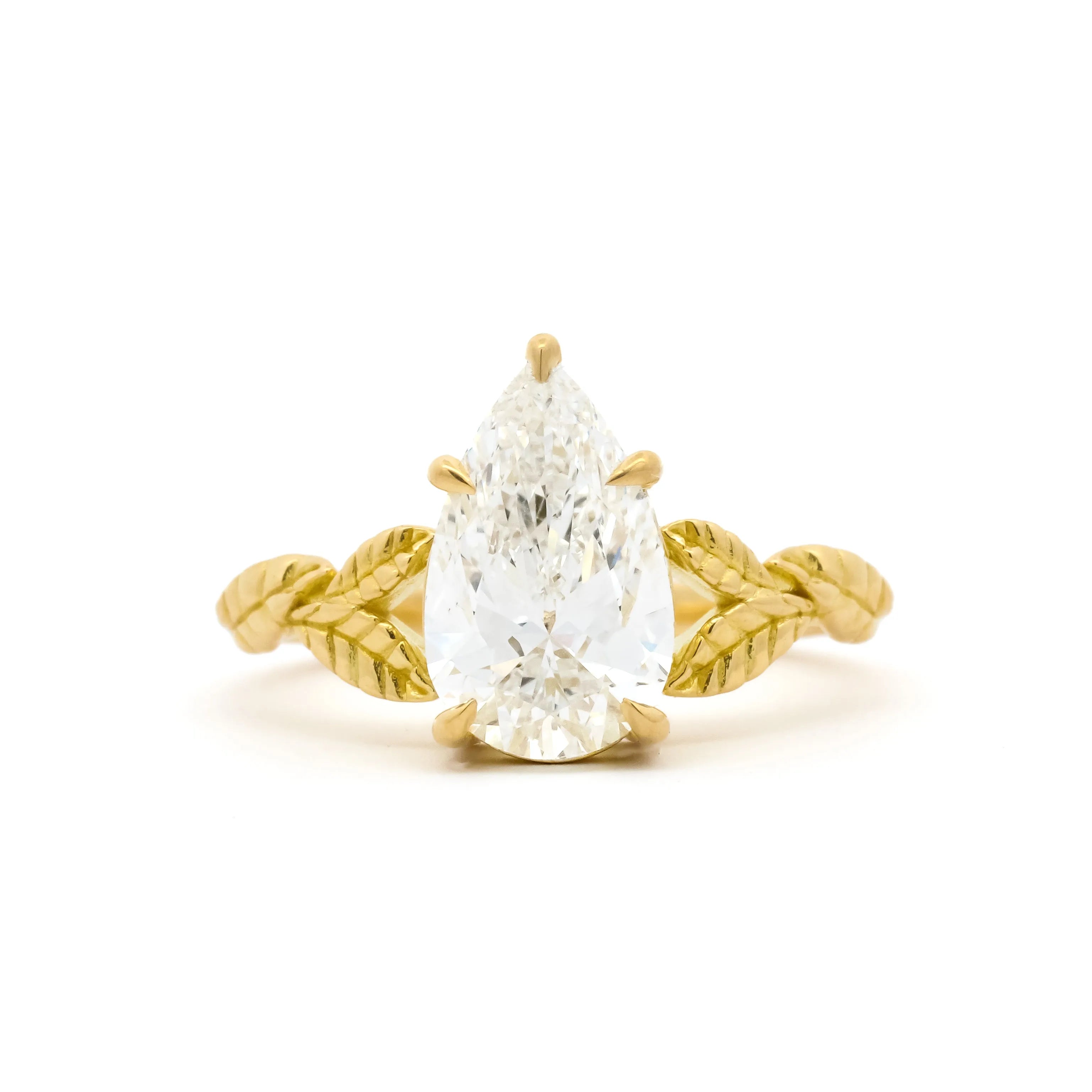 gold engagement ring with leaf detail on band and large pear diamond on a white background