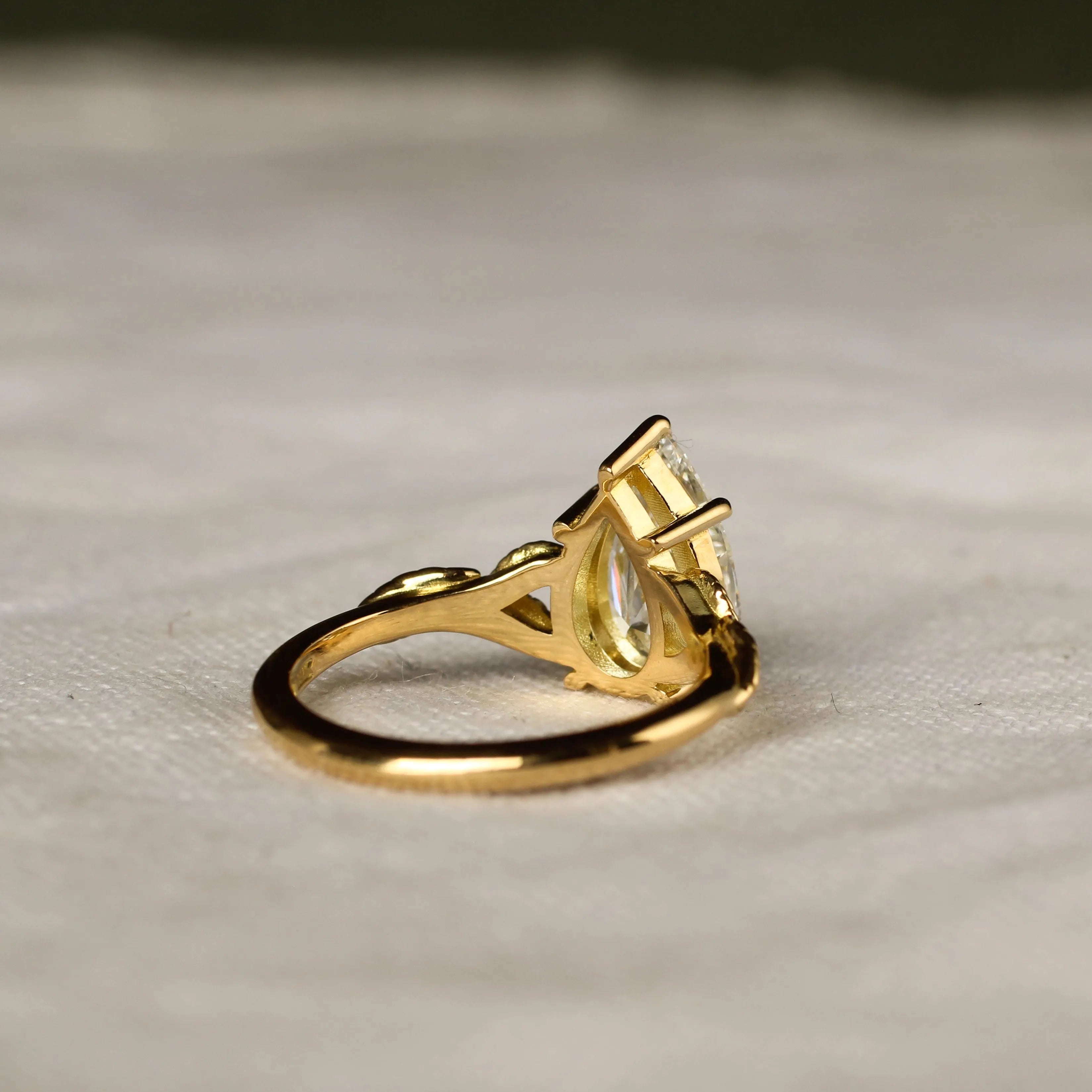 back view of pear engagement ring with leaf detail on a beige fabric