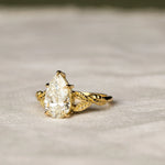 engagement ring with leaves on band and pear diamond on a neutral fabric