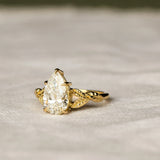 engagement ring with leaves on band and pear diamond on a neutral fabric